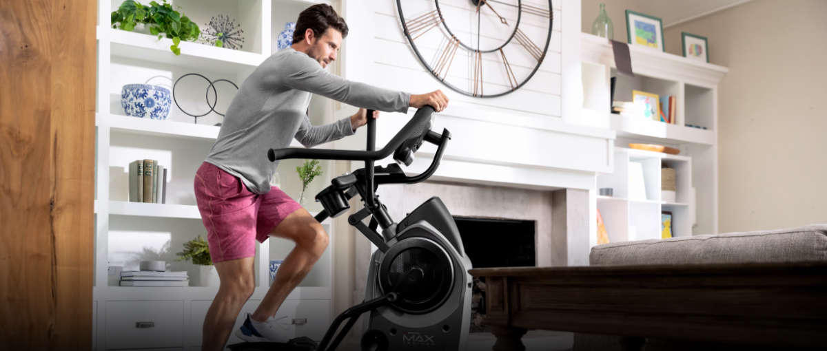 A man getting a workout using a Max Trainer compact elliptical located in the corner of a room.